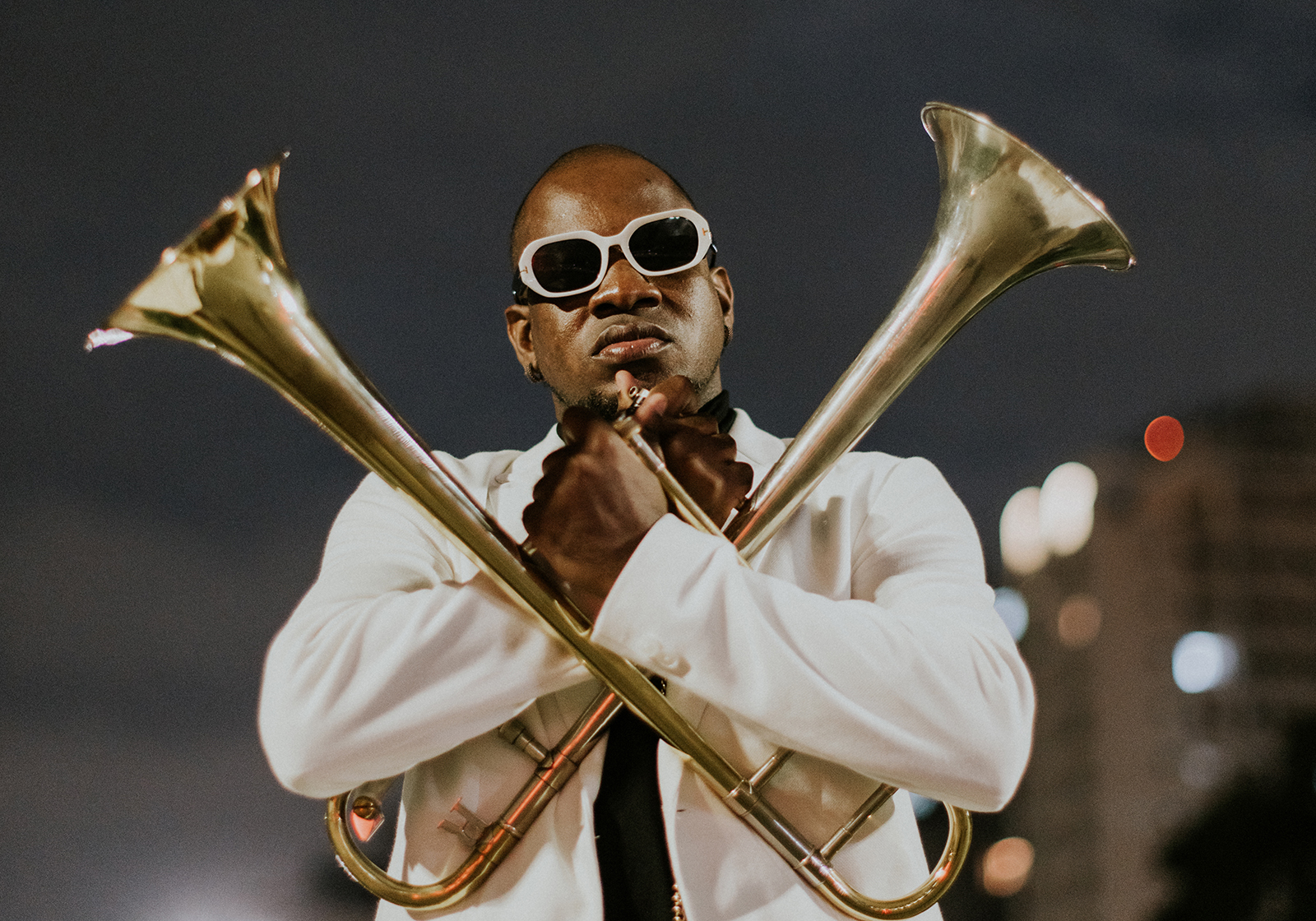 Joabe Reis in white suit, with two trombones held across his body