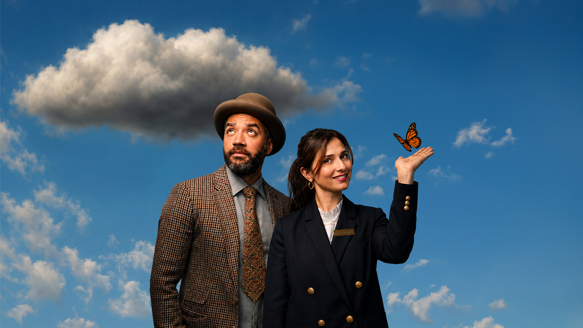 One Mixed race man in a brown tweed jacket and brown bowler hat looks up to a grey cloud in the sky. Next to him, a woman in a navy jacket with gold buttons looks into the camera as an orange butterfly lands on her hand. 