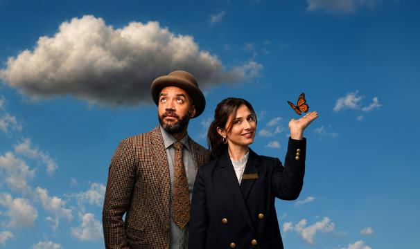 One Mixed race man in a brown tweed jacket and brown bowler hat looks up to a grey cloud in the sky. Next to him, a woman in a navy jacket with gold buttons looks into the camera as an orange butterfly lands on her hand. 